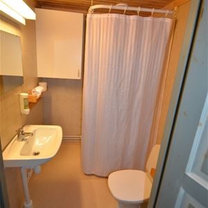 Badrum med gula väggar och golv, dusch, toalett och handfat.