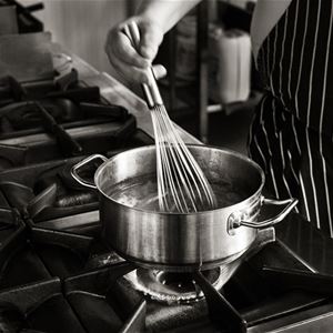 hand whisking in a saucepan on a gas stove.