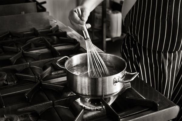 hand whisking in a saucepan on a gas stove. 
