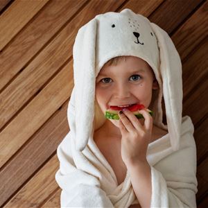 Ett barn i badrock som äter melon. 