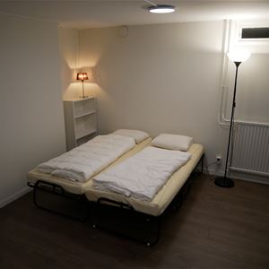 Två resesängar i ett rum med vita väggar och mörkt golv.
