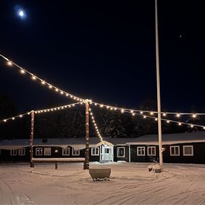 Hotellet vid fjället utvändigt en vinterkväll, upplyst av ljusslingor mellan husen. 