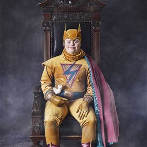 Foto: Emma Svensson,  © Copy: Glad Hudik teatern, En person som sitter i en tronstol och ahr superhjälte köder på sig.