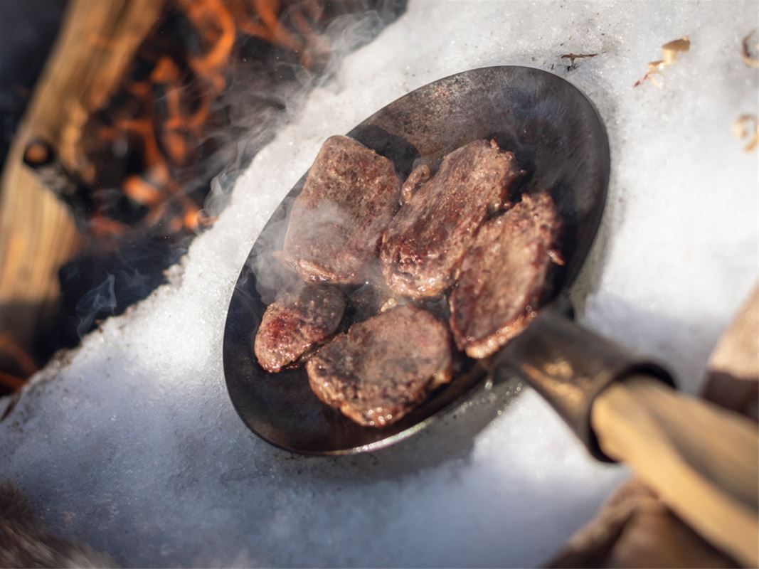 Frying pan with pieces of meat that are fried outdoors.