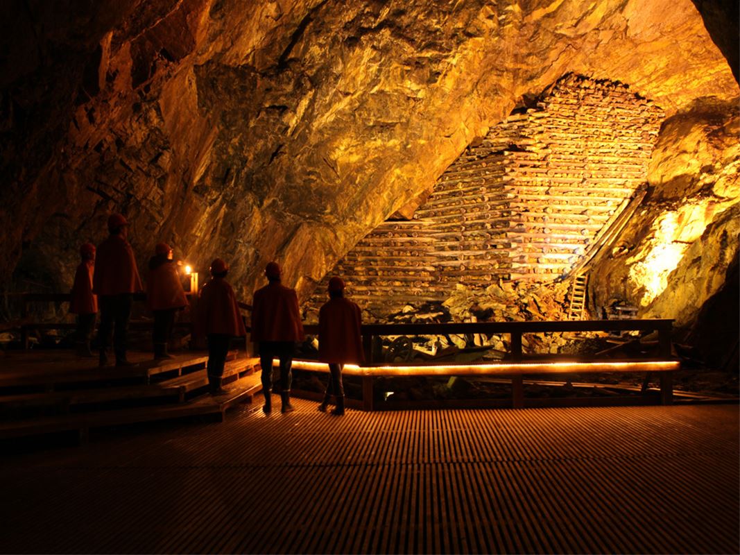 En grupp personer går i ett stort gruvrum under jord.