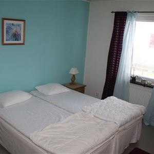 A double bed in a bedroom with light blue walls and light blue and black curtains. 