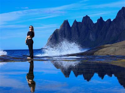 Person poserer ved kysten med fjell i bakgrunnen