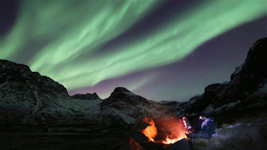 Et bål med gjester rundt under nordlys
