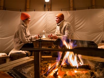 Gjester hygger seg ved bålet inne i lavvoen