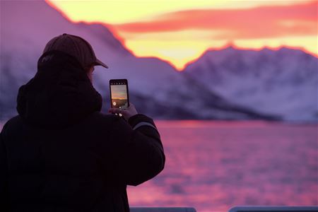Person som fotograferer utsikt over fjell og arktisk lys på en hvalsafaritur med Rødne Fjord Cruise i Tromsøregionen