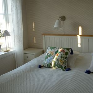 Dubbelsäng med vitt överkast och blommiga kuddar på sängen. 