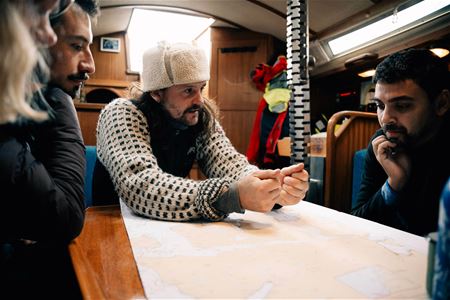 People around a table with a map in a boat cabin