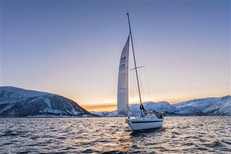 Sailboat with people on board in front of snow-covered mountains