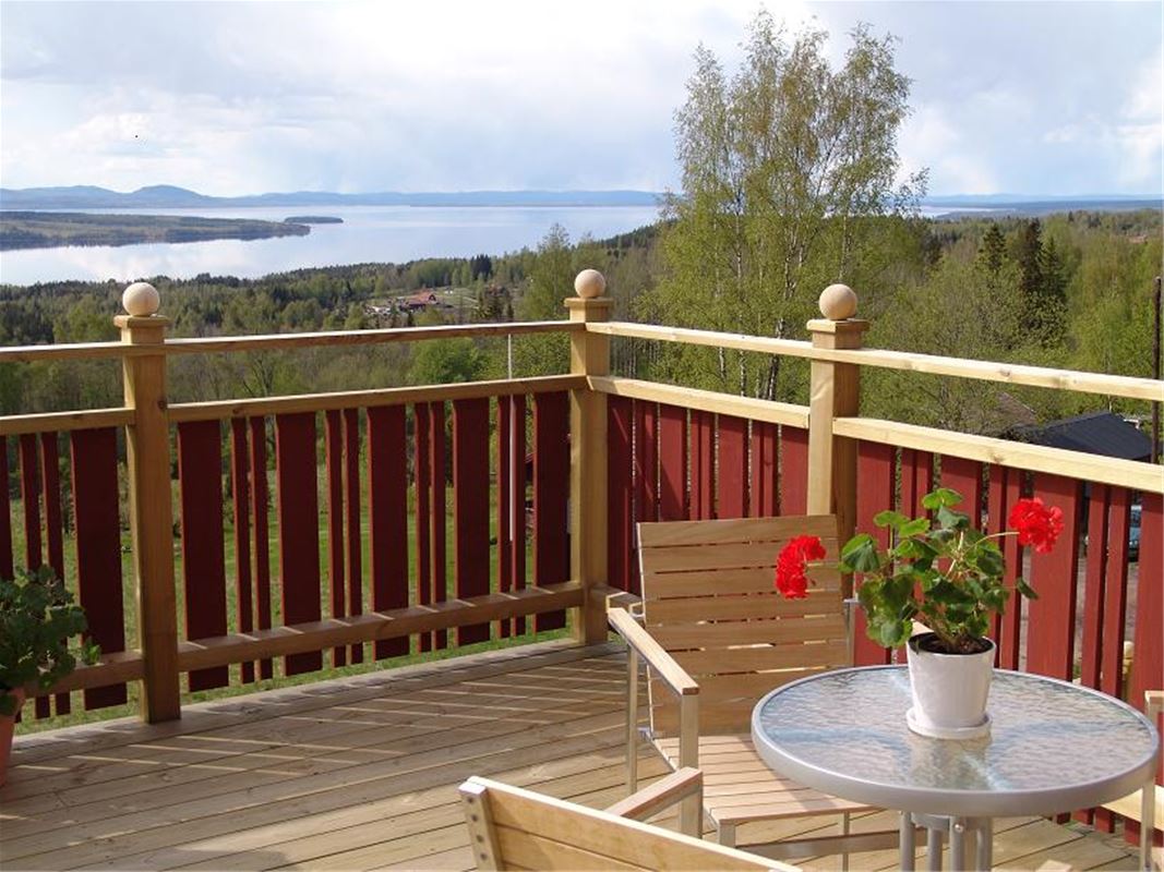 Balkong med rödmålat räcke och utsikt över sjön SIljan. 