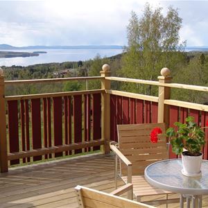 Balkong med rödmålat räcke och utsikt över sjön SIljan. 