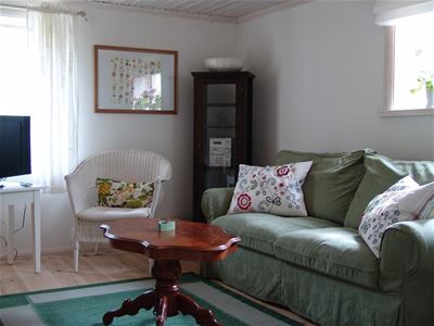 Grön soffa, vit fåtölj och ett litet runt  soffbord.