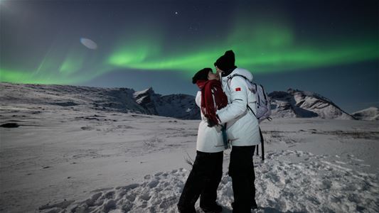 Two people kissing under the northern lights