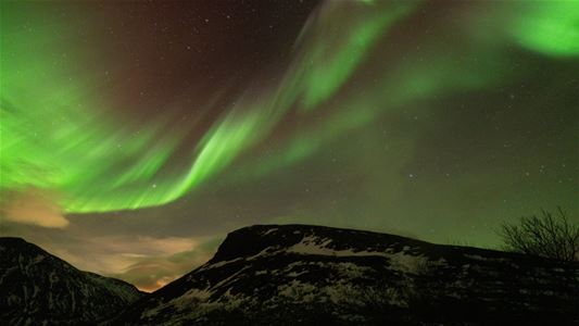 Green northern lights in the sky above mountains