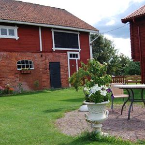 Large barn in two floors with upper floor in red panel and lower floor in red brick and garden furniture in the garden.