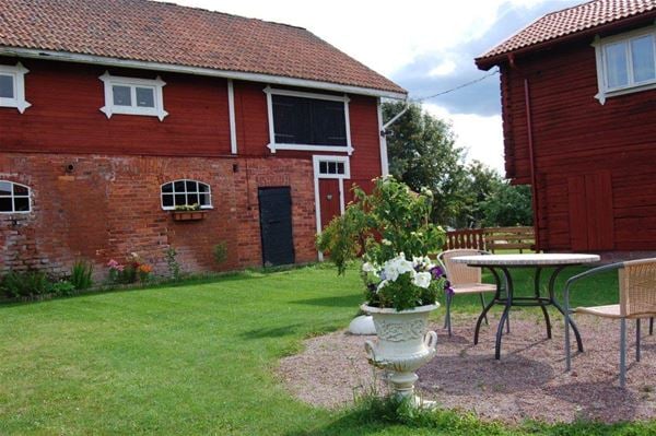 Large barn in two floors with upper floor in red panel and lower floor in red brick and garden furniture in the garden. 