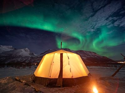 Glødende telt i snødekt landskap under nordlys.