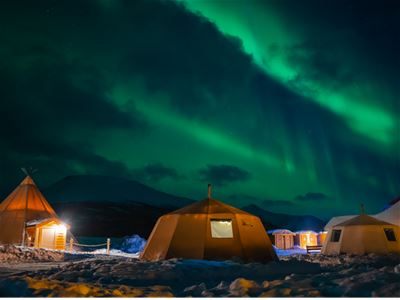Telt i snødekt landskap under nordlys om natten.
