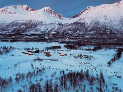 Snødekt landskap med teltleir og fjell i bakgrunnen.