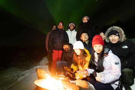Gjester sitter bak bålet og foran auroa borealis