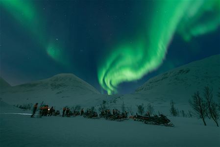 Gjester står ved snøskuterne og beundrer det vakre nordlyset