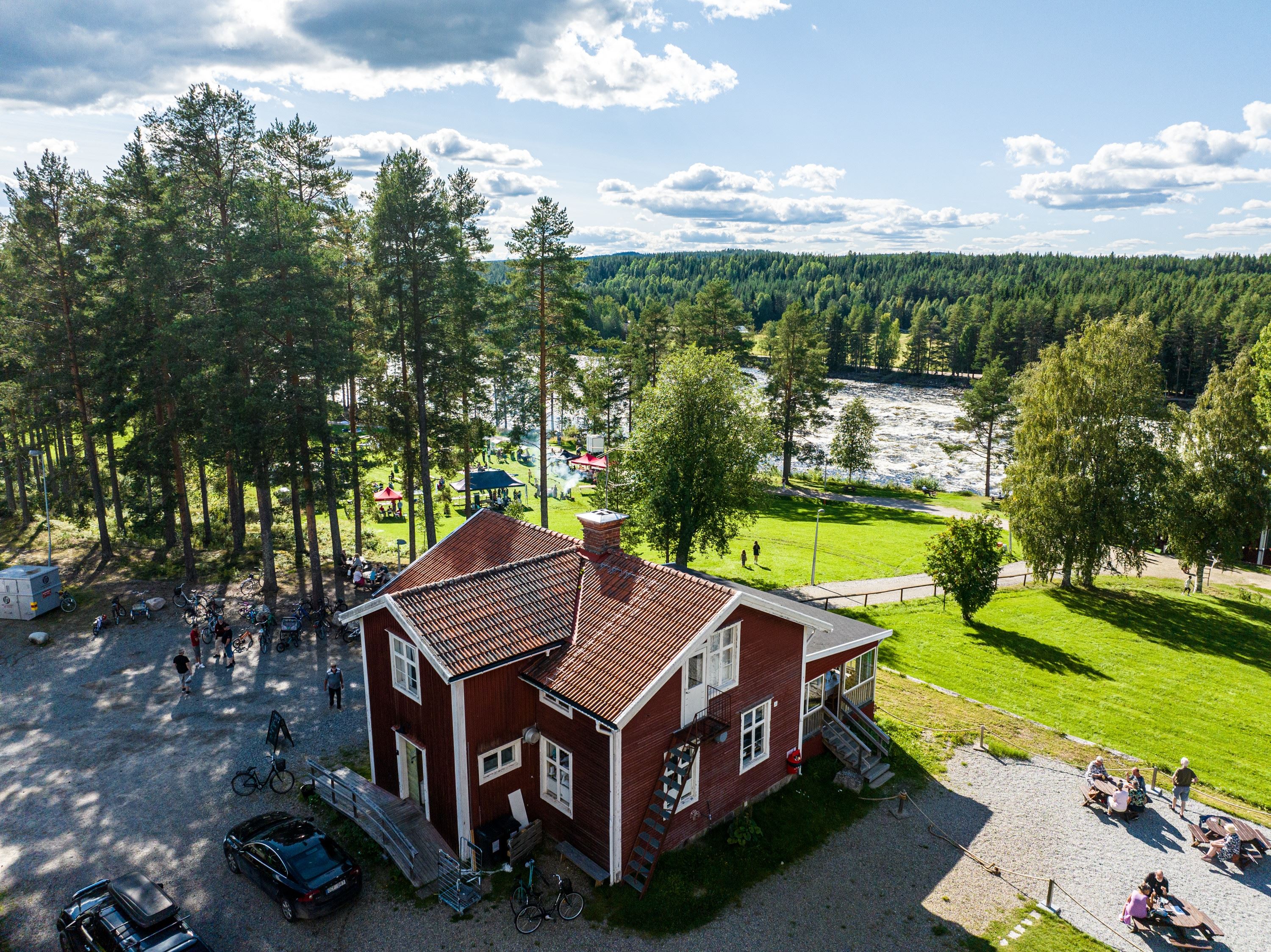 rött hus med vita knutar beläget invid en älv och gröna ängar
