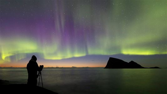 Person som tar bilde av nordlys ut mot kysten