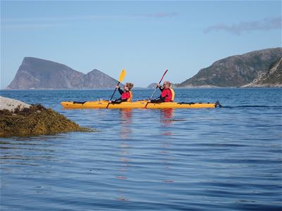 A couple paddle in the sea with the famous Håja mountain in the background