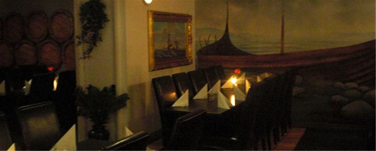 Interiörbild från restaurangen, ett uppdukat bord med vita servetter, tända ljus på bordet, bruna skinnstolar, en tavla med guldram på väggen.