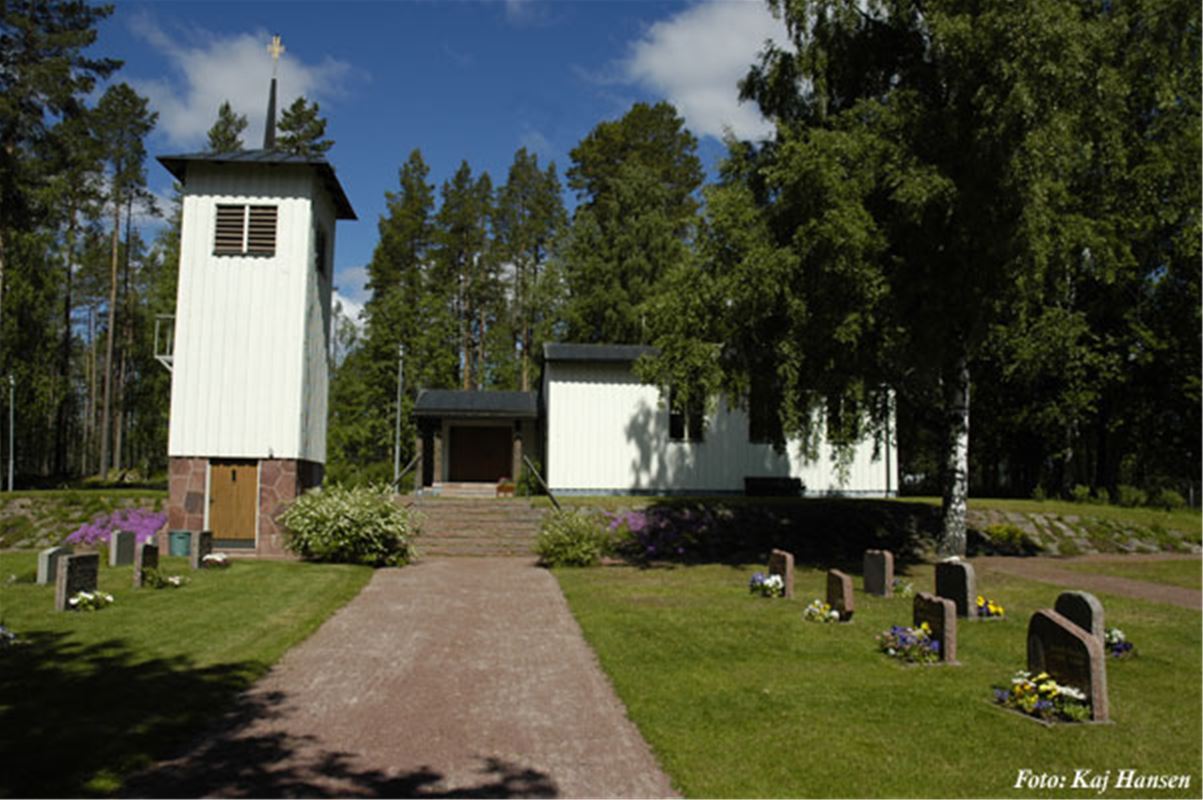 A small white chapel with trees and some graves