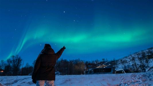 A person pointing towards Northern Lights in the sky