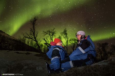 Two guests sitting under the northern lights