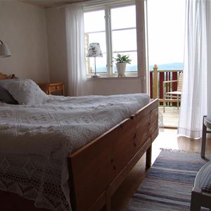 Double bed with white bedspread and white curtains in fron of an open door to the balcony.