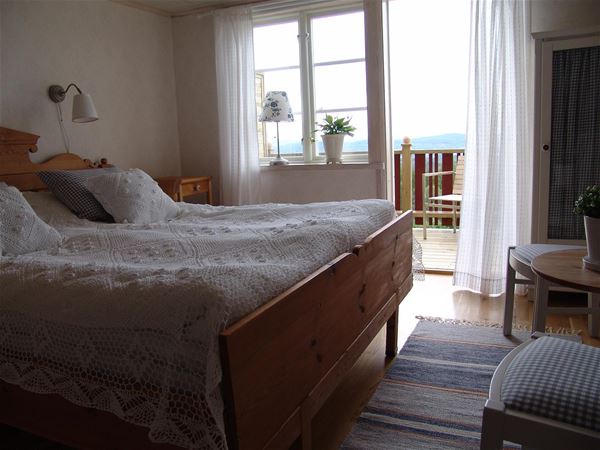 Double bed with white bedspread and white curtains in fron of an open door to the balcony. 