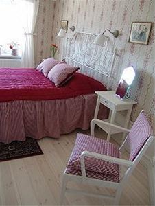 Double bed with pink bedspread and floral wall paper in the room. 