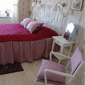 Double bed with pink bedspread and floral wall paper in the room. 