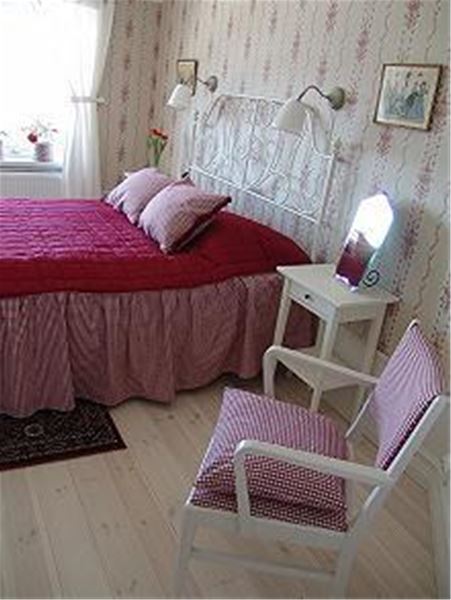 Double bed with pink bedspread and floral wall paper in the room.  