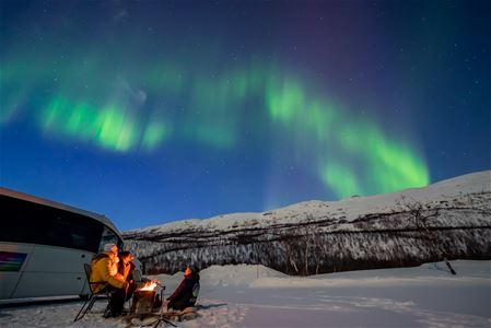 Northern lights and guests around campfire
