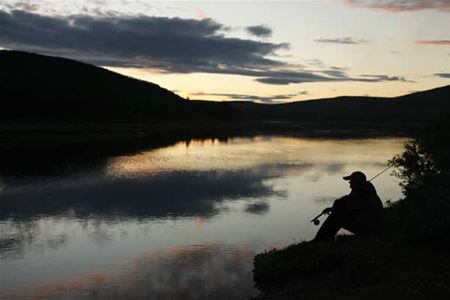 Stilla kväll vid sjön där fiskare sitter på strandkanten med fiskespö på axeln.