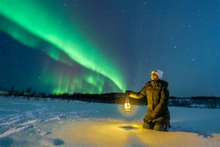 A person holding a lamp under the Northern Lights