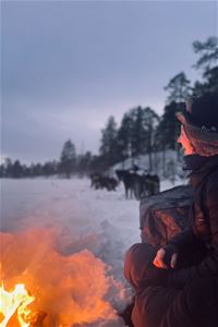 A guest sitting near a bonfire
