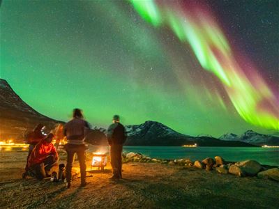 Guests sit by the fire and relax while the Northern Lights dance above