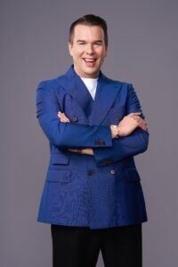 En leende man i blå kavaj med armarna i kors.