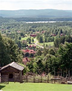 View from Dössberget, road that winds through village with red log houses, lake and mountains in the background.