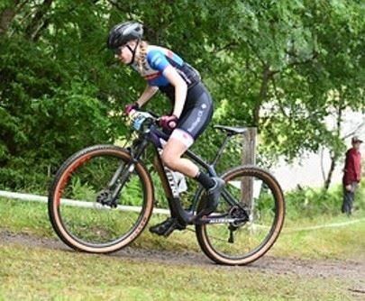 Cyklist med hjälm och sportkläder cyklar en mountainbike på grusväg i grön skogsmiljö..