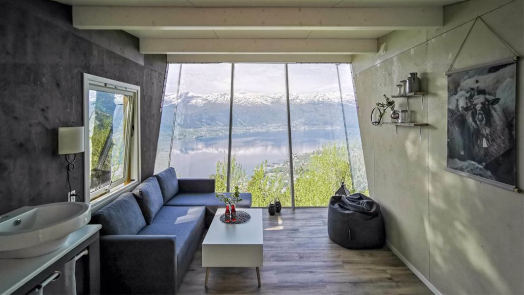 Lys stove med sofa og salbord, stor panoramavindauge mot fjord og snødekte fjell, beanbag på golvet..